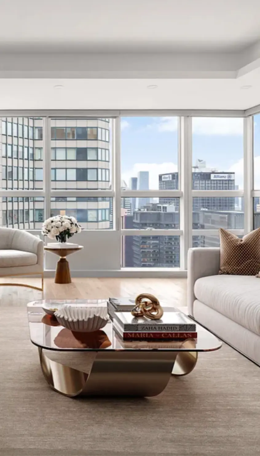 Luxury Manhattan living room with floor-to-ceiling windows showcasing city skyline views, featuring modern neutral-toned furniture, gold accents, and designer décor — representing high-end New York real estate.