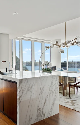 Luxury New York City condo kitchen with floor-to-ceiling windows, marble waterfall island, and panoramic Hudson River views."