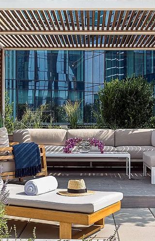 Rooftop terrace in New York City featuring modern outdoor lounge furniture, wood pergola, and skyline reflections on glass building.